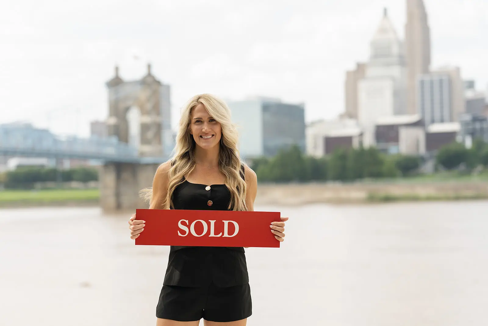 Lauren Wessel holding a sold sign with the Cincinnati skyline behind her
